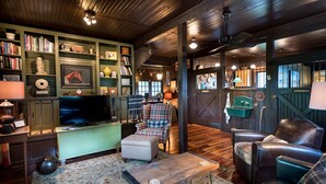A cozy living room with a television, bookshelves, leather chairs, and a patterned rug.