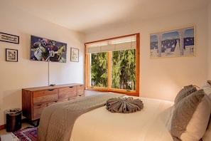 Une chambre à coucher avec un grand lit, une commode en bois et une fenêtre avec des stores.