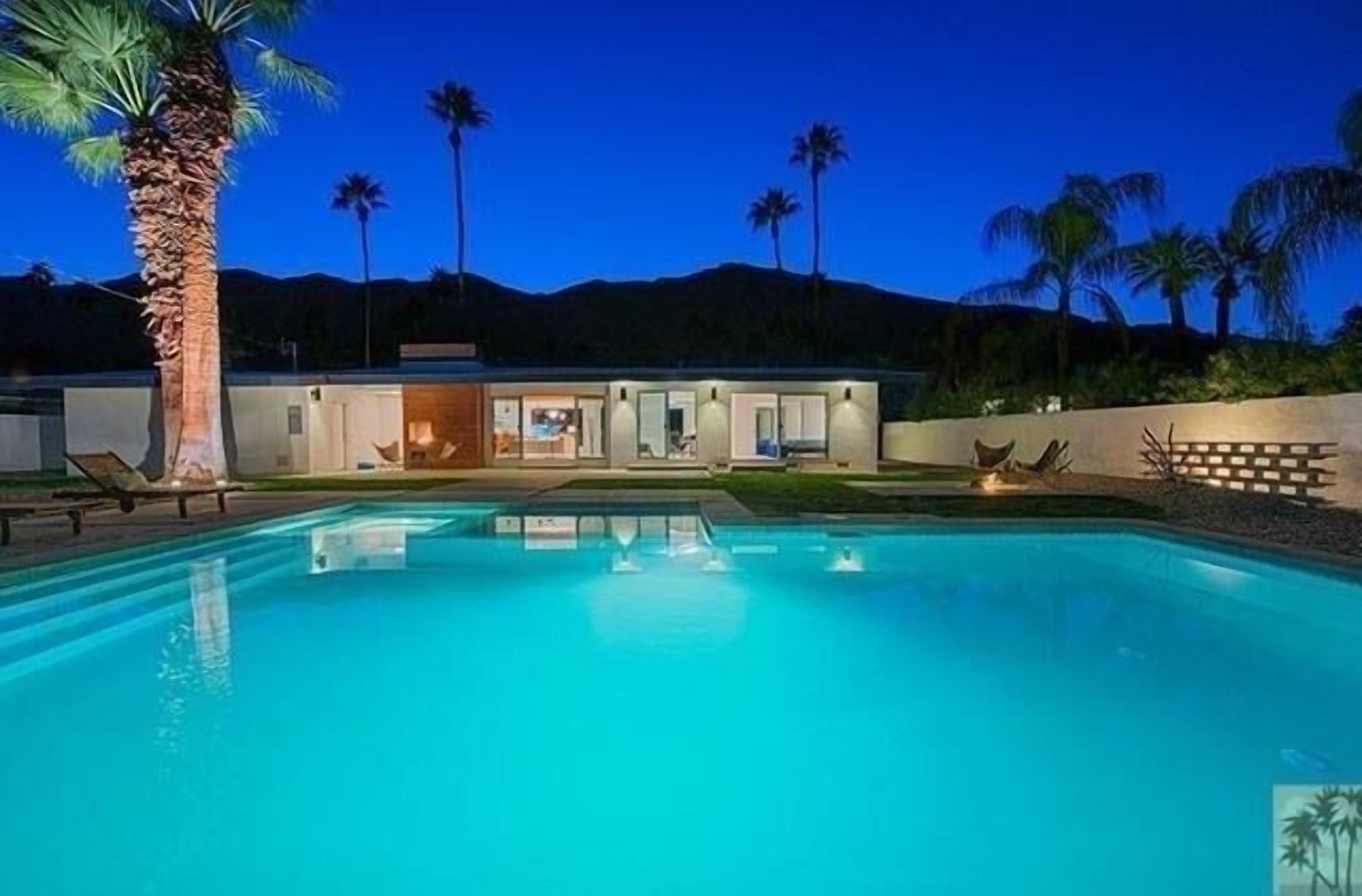 A modern house with a swimming pool, palm trees, and a mountain backdrop.