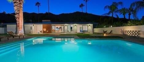 A modern house with a swimming pool, palm trees, and a mountain backdrop.