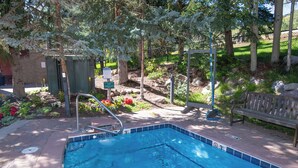 Piscina con una escalera metálica, rodeada de árboles y una banca.