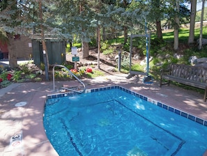 A rectangular pool with a tiled edge, a metal ladder, a bench, and a sign indicating 'SPA RULES' near a tree.