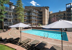 A swimming pool with lounge chairs and umbrellas, surrounded by a brick patio.