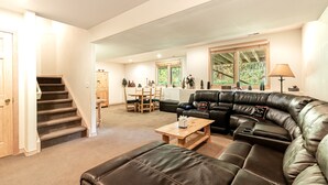 A spacious living room with a black leather sofa, a wooden coffee table, and a staircase leading to another level. - Spacious 4BR Townhome | 2 Living Rooms and Walk to Ski Area! (Steamboat Springs)