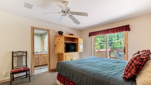 A bedroom with a bed, a television, a wooden cabinet, a chair, and a balcony with a view of trees. - Spacious 4BR Townhome | 2 Living Rooms and Walk to Ski Area! (Steamboat Springs)