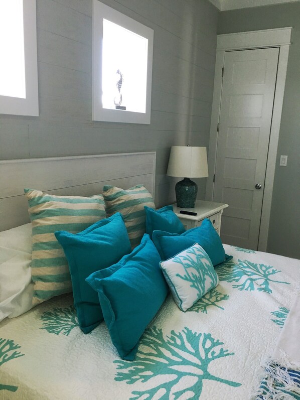Un dormitorio con cama, almohadas, mesita de noche, lámpara y puerta.