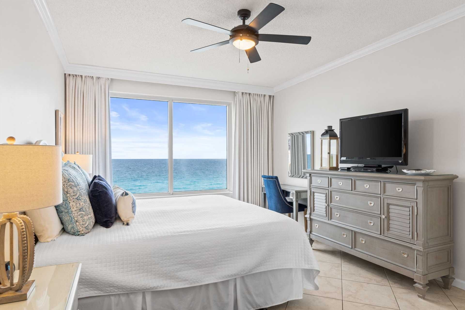Een hotelkamer met een bed, een televisie, een dressoir en uitzicht op zee.