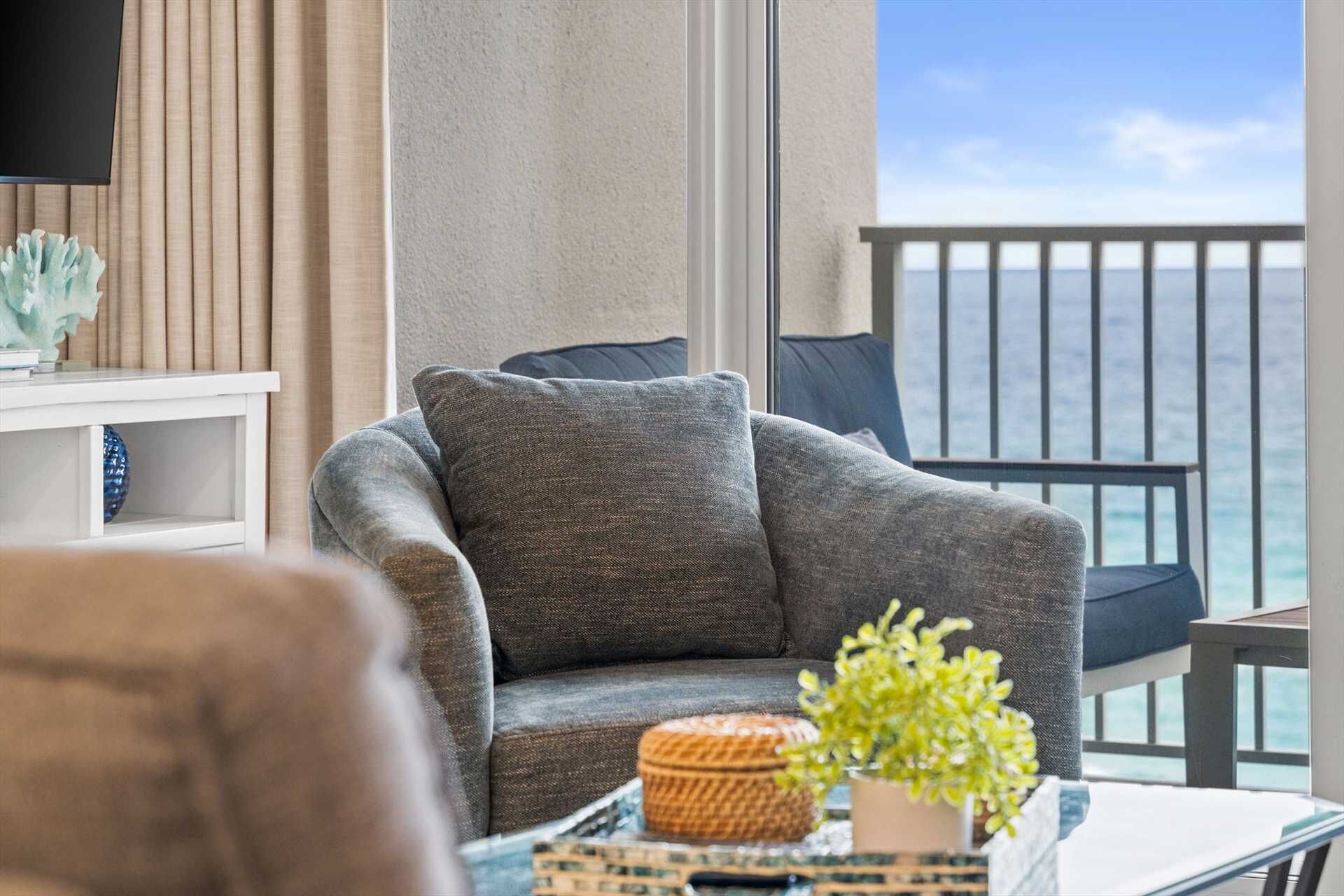 Un balcon avec vue sur l’océan, un fauteuil gris, une petite table avec une plante et un panier en osier.