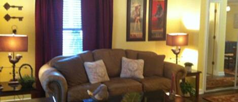 A living room with a brown sofa, two side tables with lamps, a coffee table, and a window with purple curtains.