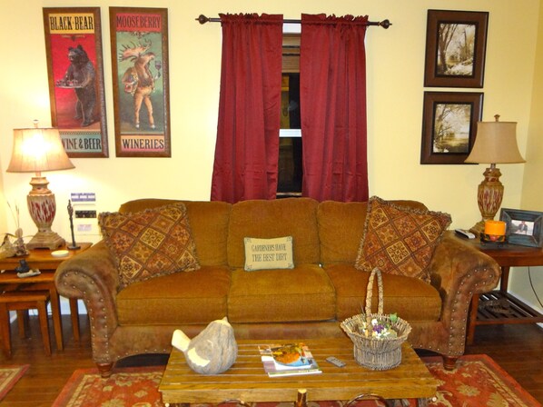 A cozy living room with a brown sofa, red curtains, and a coffee table with a basket. - Aspen Suite: Cozy NC Mountain & Riverside Cabin Suite @ Roaring River Vineyards (Traphill)