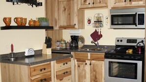 A kitchen with wooden cabinets, a granite countertop, a microwave, an oven, and various kitchen utensils. - Aspen Suite: Cozy NC Mountain & Riverside Cabin Suite @ Roaring River Vineyards (Traphill)