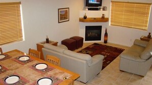 Un salon avec une cheminée, un téléviseur et un coin repas avec une table mise pour quatre personnes.