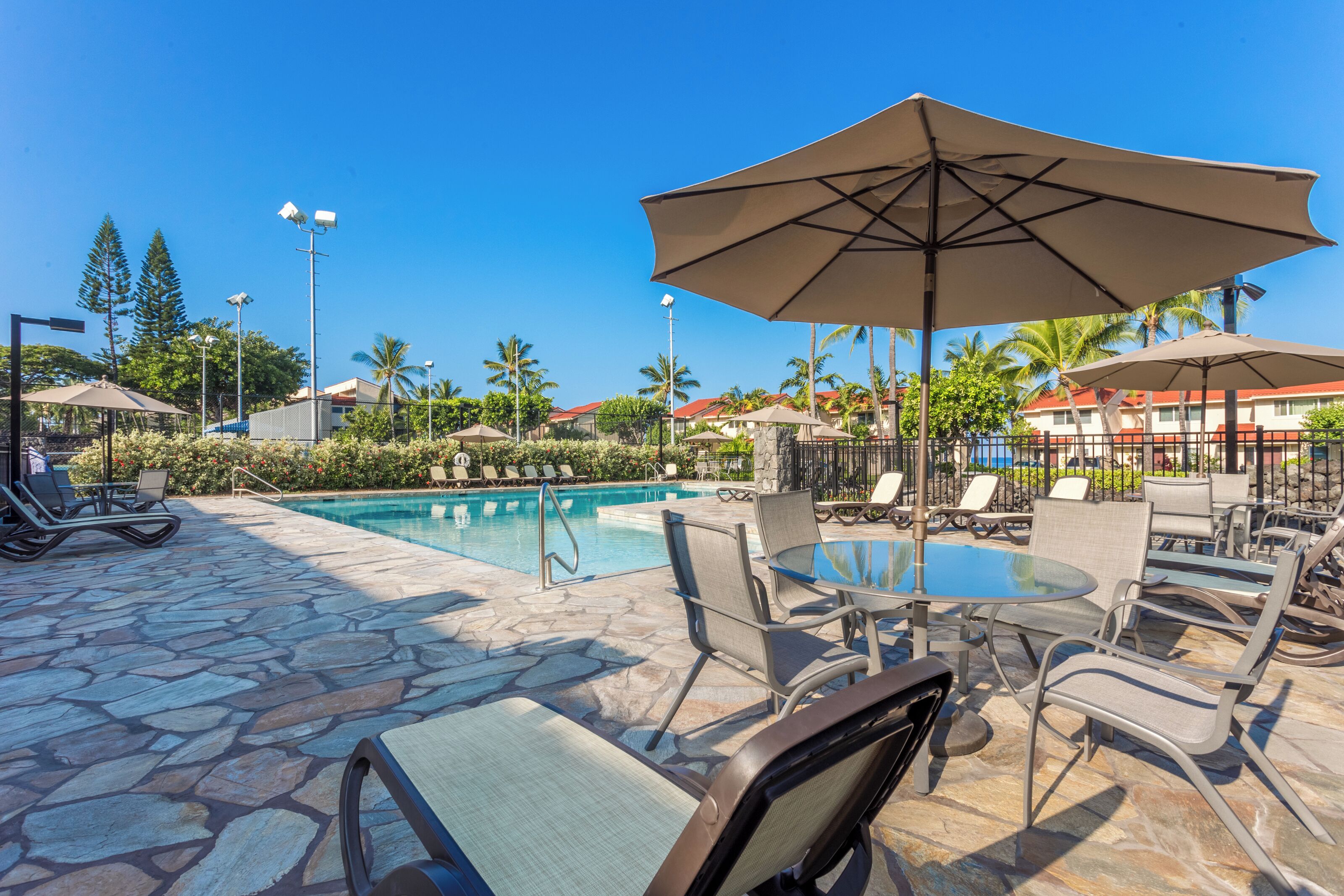 A poolside area with lounge chairs, umbrellas, and a stone-tiled floor.