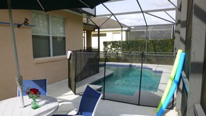 Une terrasse couverte avec une piscine, une table ornée d’un vase de fleurs et une chaise.