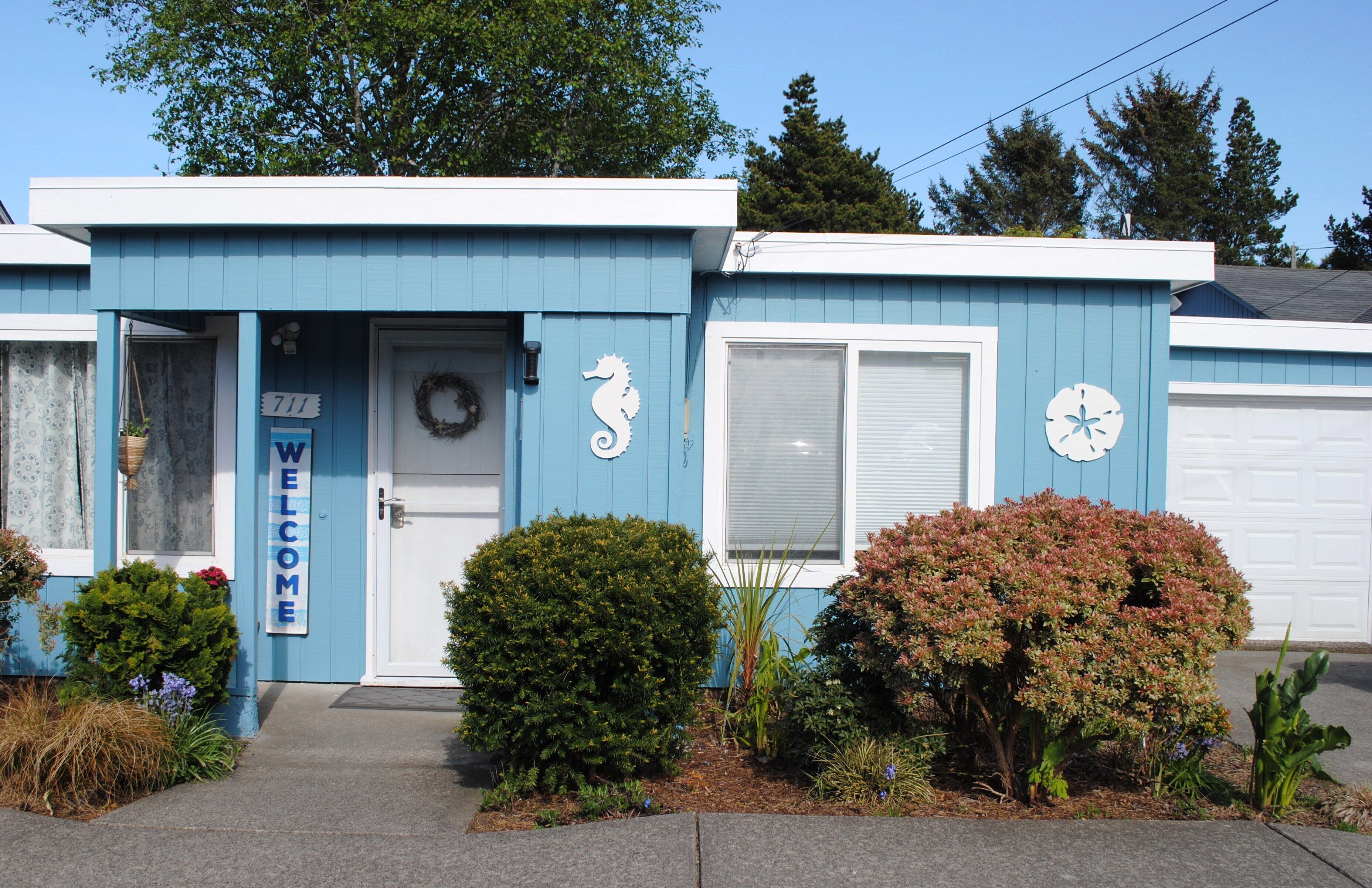 A blue building with a 'WELCOME' sign, a wreath, a seahorse decoration, and a clock.