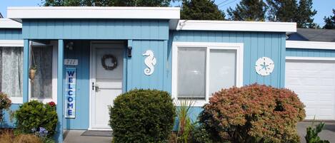 A blue building with a 'WELCOME' sign, a wreath, a seahorse decoration, and a clock.