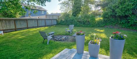 Een achtertuin met een houten terras, een vuurkorf en potplanten.