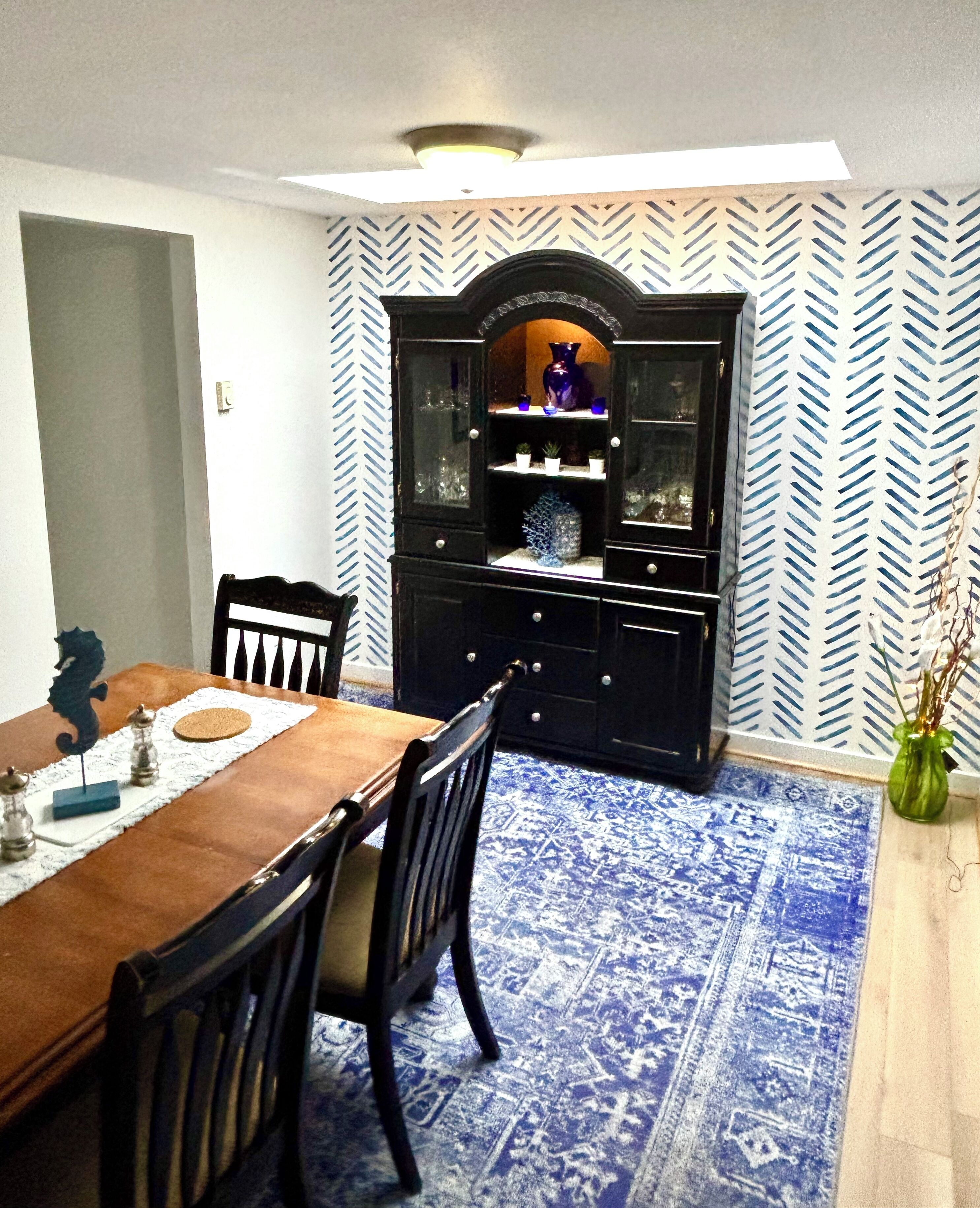 A dining area with a wooden table and chairs, a patterned rug, and a black cabinet with glass doors.
