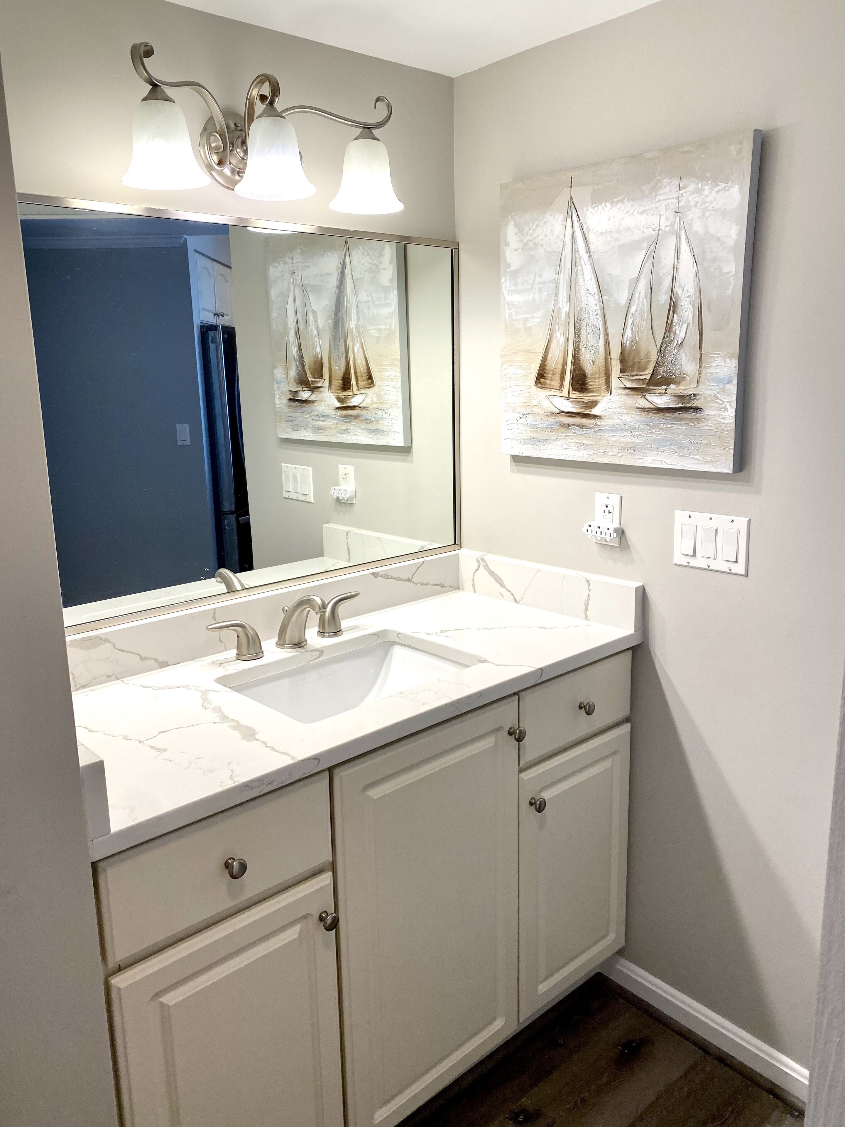 Ein Badezimmer mit zwei Waschbecken, einem großen Spiegel und einem Gemälde mit Segelbooten an der Wand.