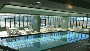 Une piscine intérieure avec des parois en verre transparent, de nombreux fauteuils et une vue sur l’extérieur.