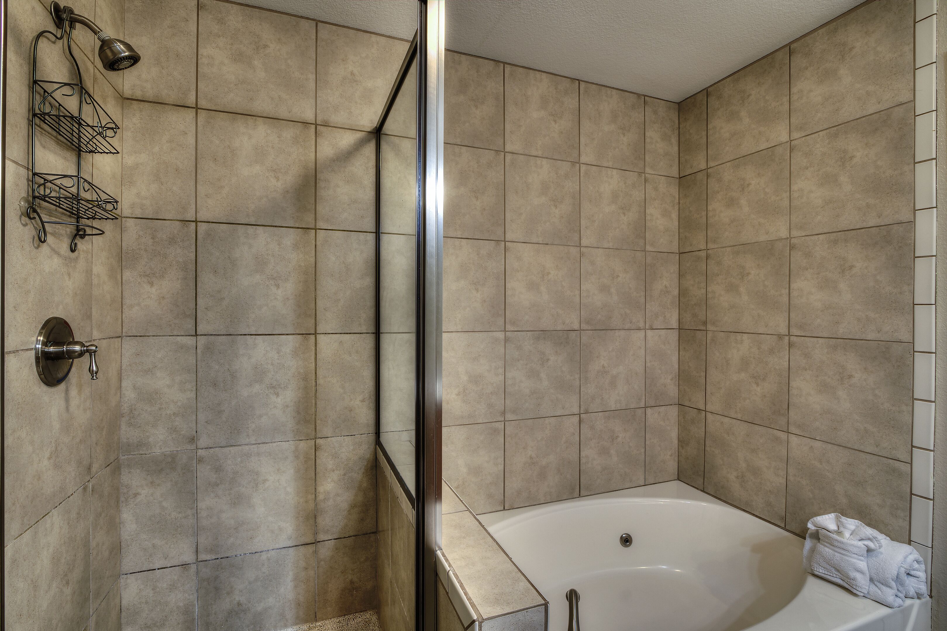 Een badkamer met beige tegels, een douchecabine van glas, een witte badkuip en een handdoek op de rand.