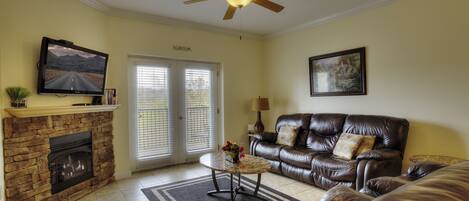 A living room with a fireplace, leather sofa, television, and a ceiling fan.