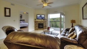 Una sala de estar con sofá de cuero, televisor, chimenea y balcón con vistas.