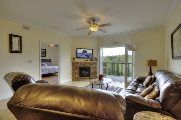 Una sala de estar con sofá de cuero, televisor, chimenea y balcón con vistas.