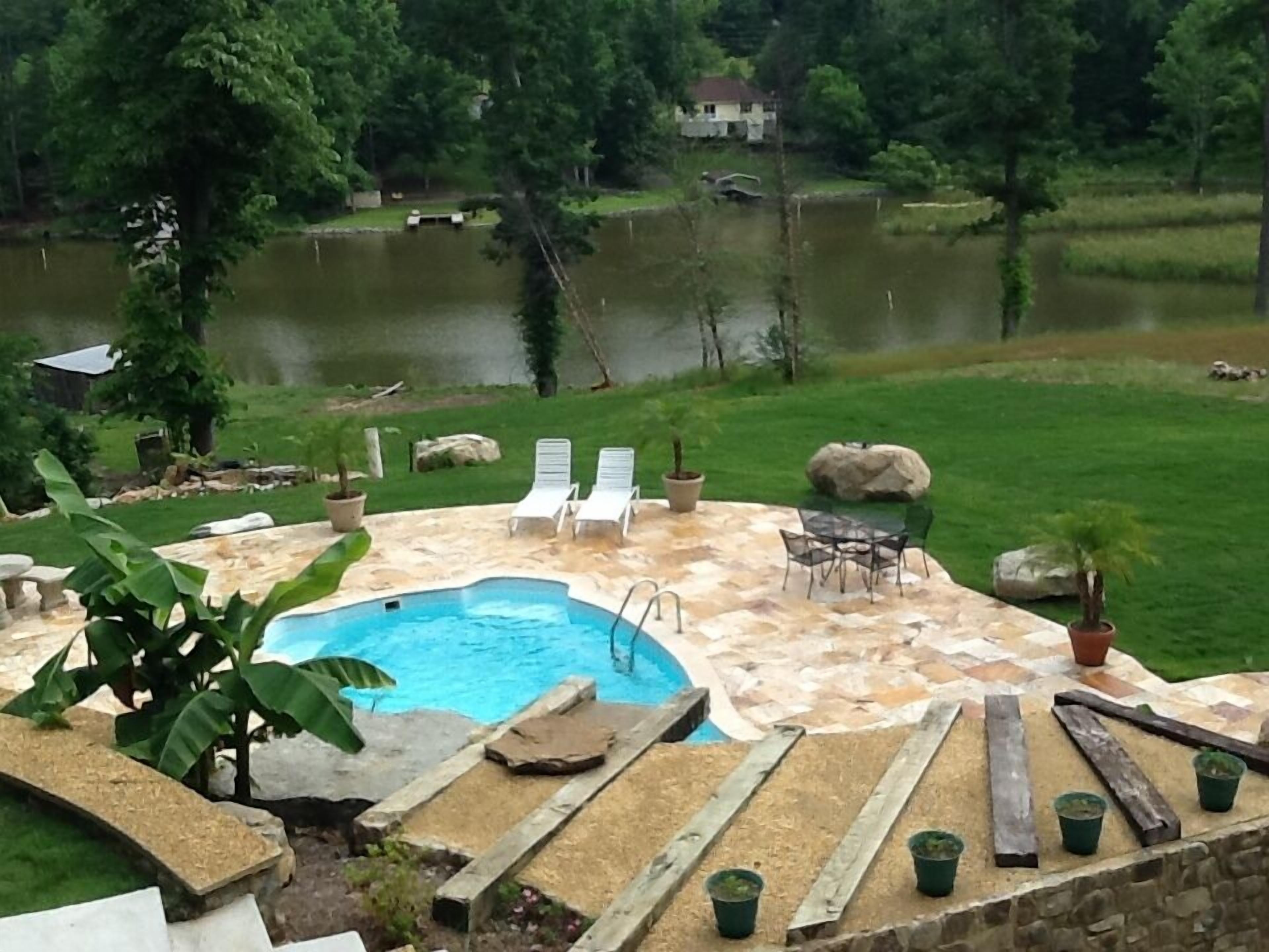 A swimming pool with a stone deck, surrounded by lounge chairs and a table.