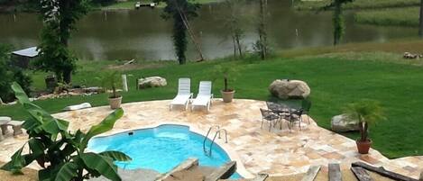 A swimming pool with a stone deck, surrounded by lounge chairs and a table.