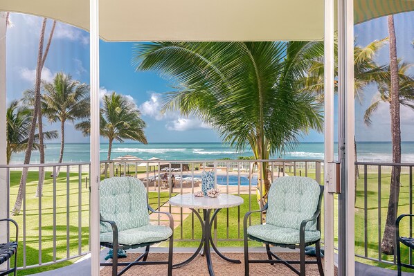 Ein Balkon mit zwei Stühlen und einem Tisch, mit Blick auf einen Pool und den Ozean.