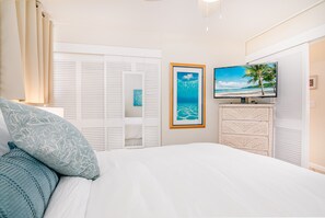 Ein Schlafzimmer mit einem Bett, einem Fernseher, einem gerahmten Bild von einem Strand und einem Kleiderschrank.