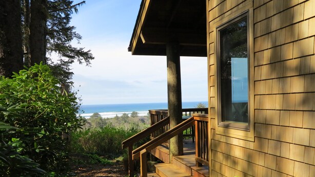 A wooden building with a deck leading to a large window overlooking a coastal landscape. - Ocean View Oasis Retreat. Comfort, plus great views! Sleeps 4. (Neskowin)