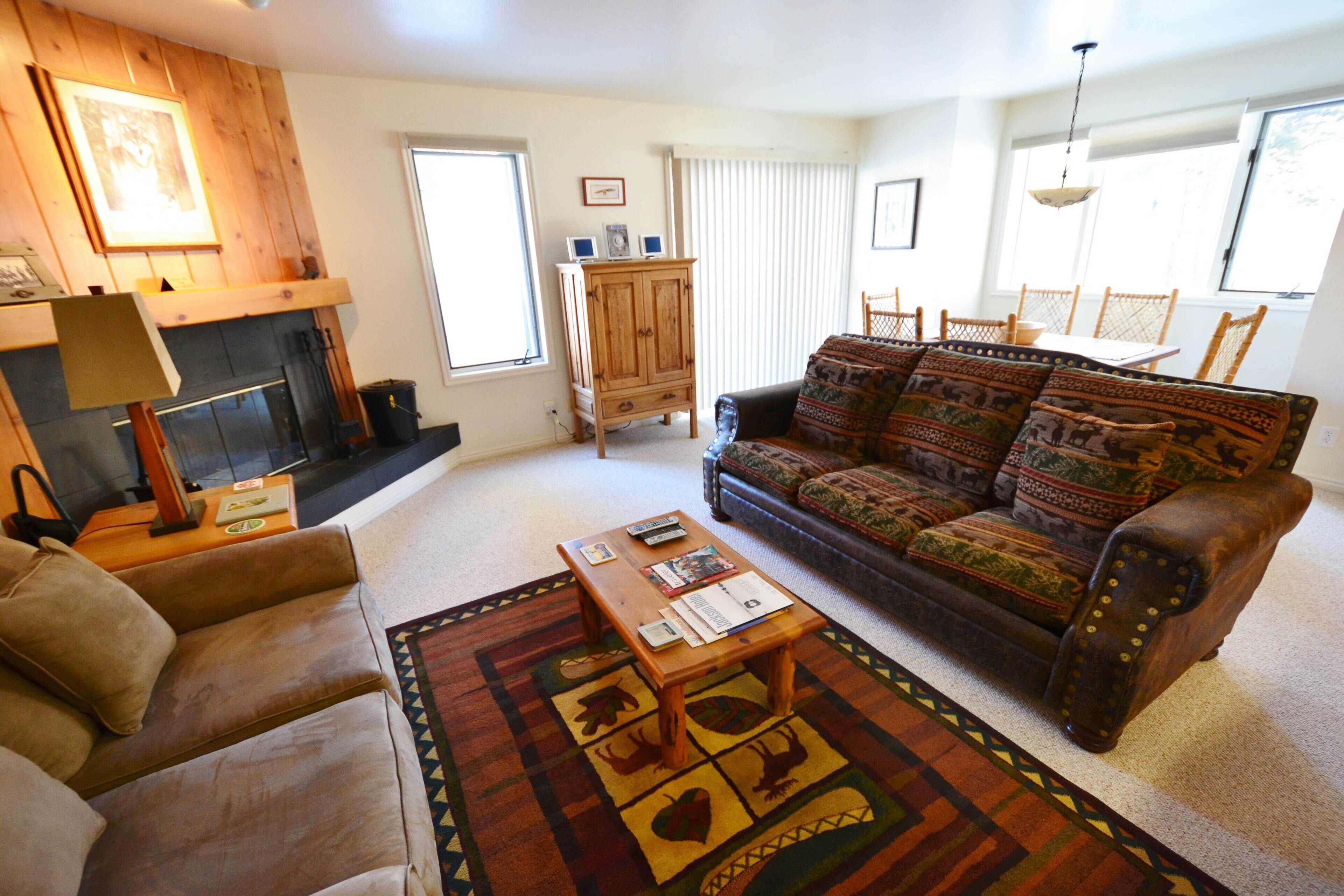 A cozy living room with a fireplace, a sofa, a coffee table, and a patterned rug.