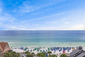 Ein Strand mit Sonnenschirmen und Personen, ein klarer Himmel und der Blick auf das Meer.