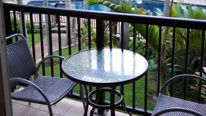 A balcony with a glass table and two chairs, overlooking a swimming pool and lush greenery. - Remodeled Condo 300 Ft From The Ocean!!!  (Koloa)