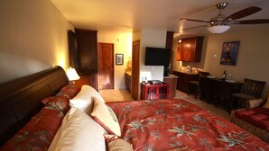 A hotel room with a large bed, a desk, a chair, a television, and a ceiling fan. - Remodeled Condo 300 Ft From The Ocean!!!  (Koloa)