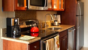 A modern kitchen with wooden cabinets, stainless steel appliances, a red kettle, and a coffee maker. - Remodeled Condo 300 Ft From The Ocean!!!  (Koloa)