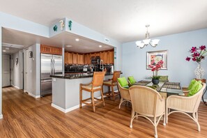 Una cucina moderna con mobili in legno, elettrodomestici in acciaio inossidabile e un'area pranzo con sedie in vimini e un tavolo in vetro.
