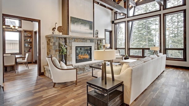 A spacious living room with a stone fireplace, white sofas, and large windows offering a view of the outdoors.