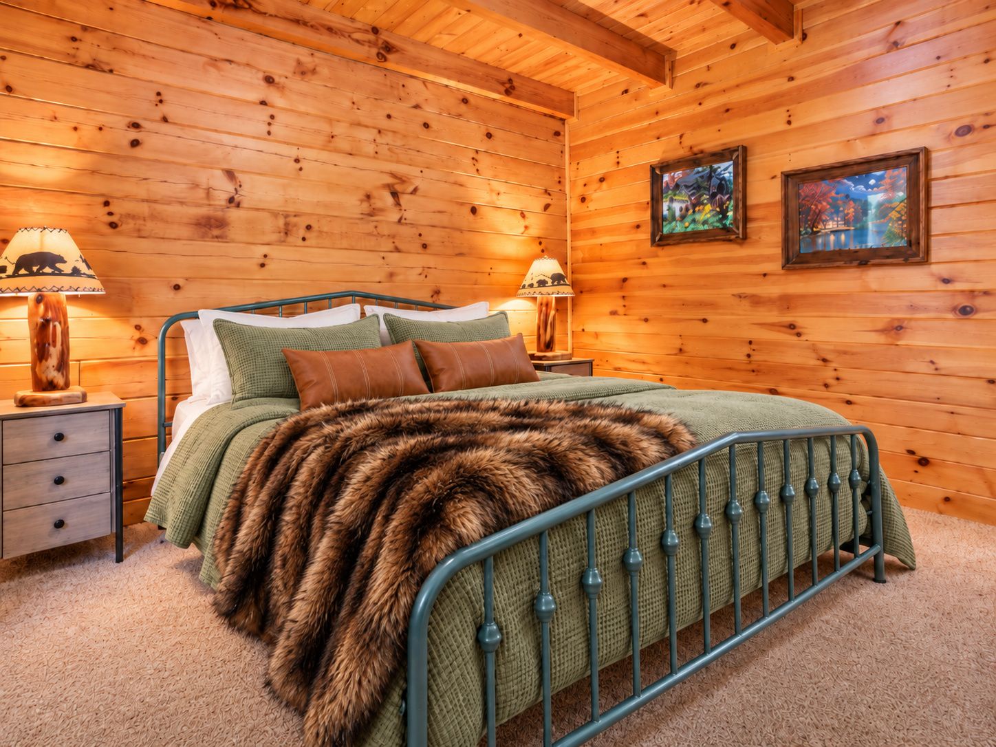 Un dormitorio de cabaña de madera con estructura de cama metálica, cubrecama verde y dos lámparas de noche.