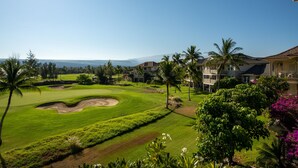A golf course with a clear view of the ocean and mountains in the distance, surrounded by lush greenery and palm trees. - Penthouse - 3 Bedrooms 2 Baths (Puako)
