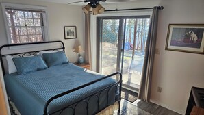 Ein Schlafzimmer mit Bett, Deckenventilator, Fenster, Tür, Teppich und einem gerahmten Bild an der Wand.