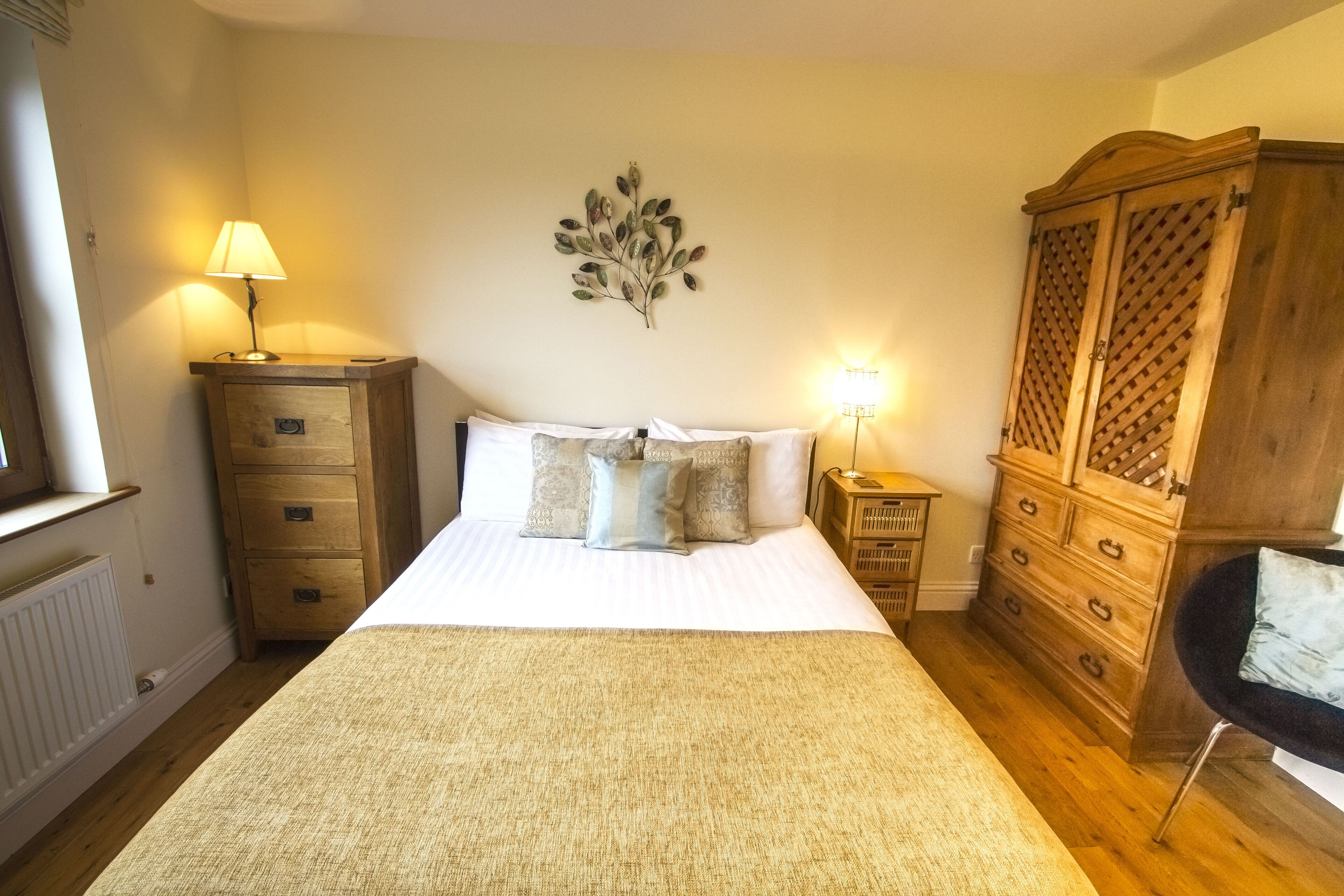 A bedroom with a large bed, wooden dresser, and a nightstand with a lamp.