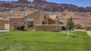 A modern house with a large window, a garage, and a well-maintained lawn in a desert landscape. - Red Rock & Mountain Views, All the Comforts of Home, Community Pool & Hot Tub (Moab)