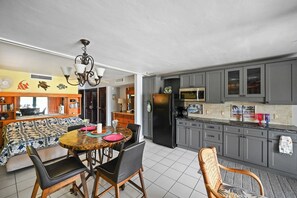 A modern kitchen with grey cabinets, a black refrigerator, and a dining area with a round table and chairs.