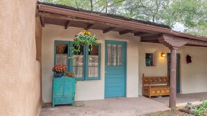 A rustic building with a blue door, a wooden bench, and a hanging flower basket. - Historic Home of Taos Artist -Peak Season Dates Available! Best Location (Taos)