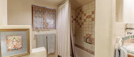 A bathroom with a shower, tiled walls, a framed picture, and towels.