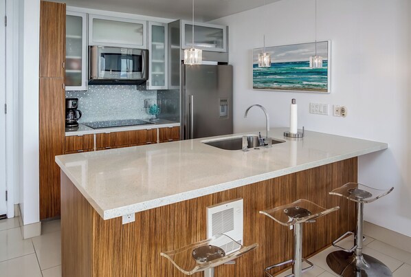 Een moderne keuken met een centraal eiland, roestvrijstalen apparatuur en een schilderij van de oceaan aan de wand.