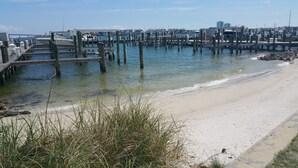 A coastal pier with boats docked, a sandy beach, and a city skyline in the background.